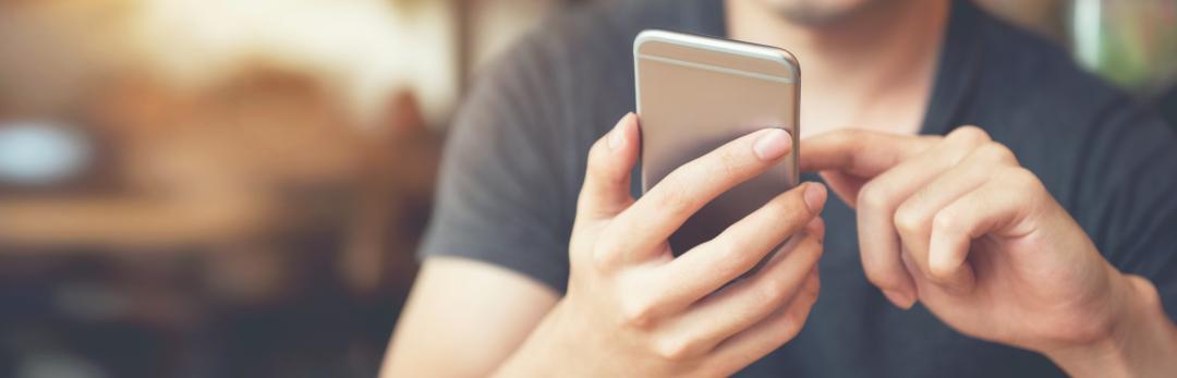 Smiling man holding a smartphone in front of him.