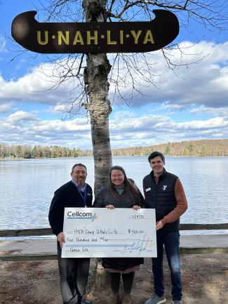 Three people holding a donation check in front of Camp U-Nah-Li-Ya sign.