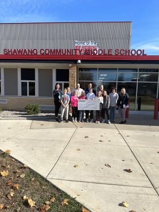 Group standing in front of Shawano Middle School holding a donation check.