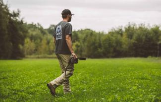 Man holding a Spartan GoLive camera while walking through a grassy area surrounded by trees.