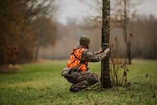 Man in blaze orange hunting vest and wearing camo attaching a Spartan GoLive camera to a tree